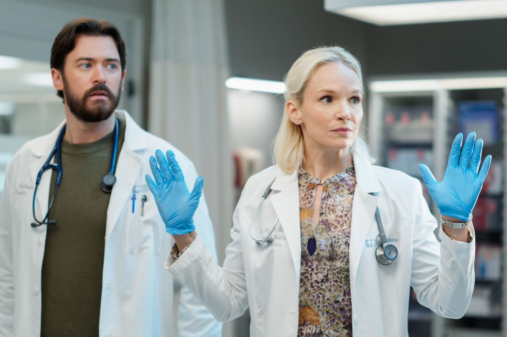 Liz raises her hands standing next to Theo in lab coats on Transplant